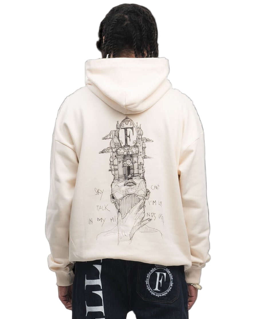 Person wearing a cream hoodie and black pants with branding on a white background